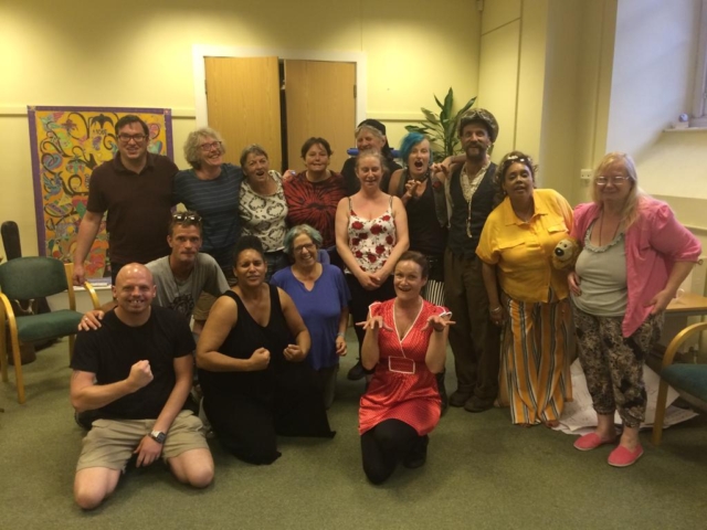 Rising Voices standing in a huddle smiling after a sea shanty workshop in 2019.