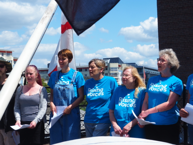 The choir wearing blue standing in a huddle performing on the SS Great Britain at Make Music Day
