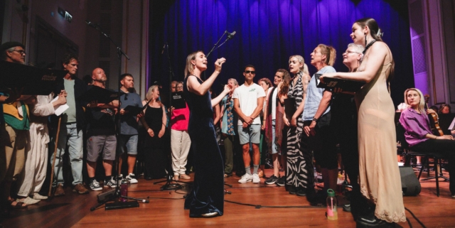 Rising Voices standing in a U shape on stage at the summer showcase at Bristol Beacon 2025