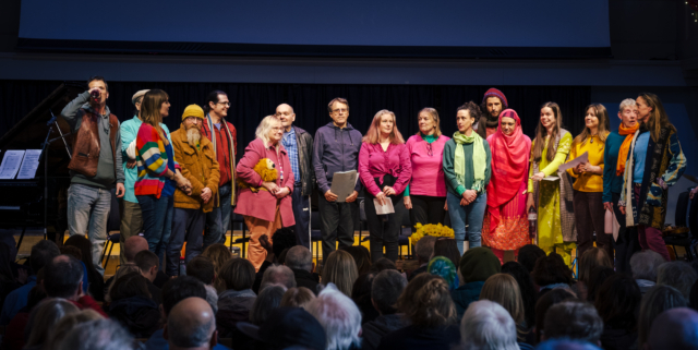 The choir standing in a line in bright colour clothes on stage performing at Maggie's memorial at St George's