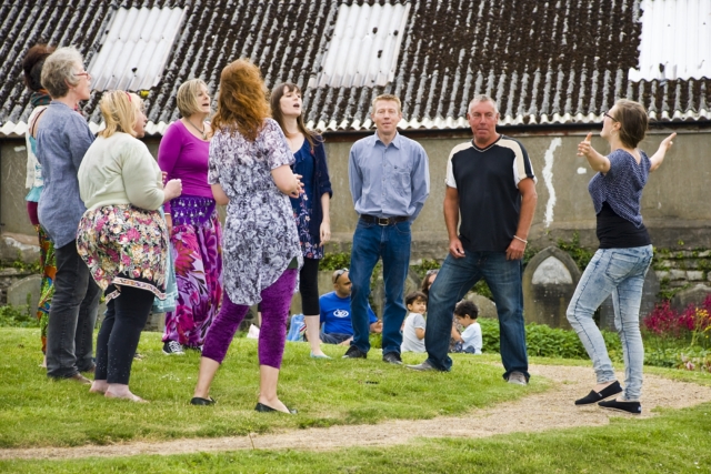 Rising Voices standing in a circle singing at their first gig in the graveyard at Brunswick Square.