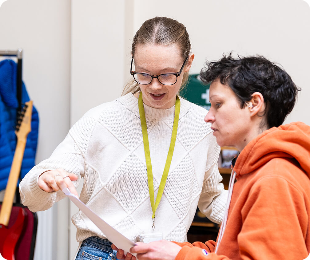 Volunteer Sophia helping a Bristol Recovery Orchestra member with their music during a rehearsal
