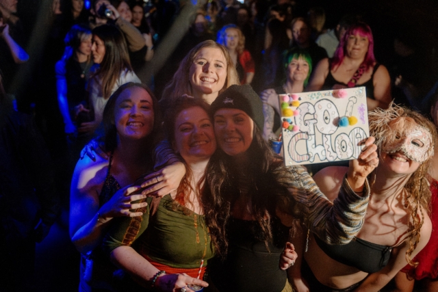 People in the crowd smiling, holding a sign to cheer on their friend Chloe playing at our sober rave at Basement 45, 2024.