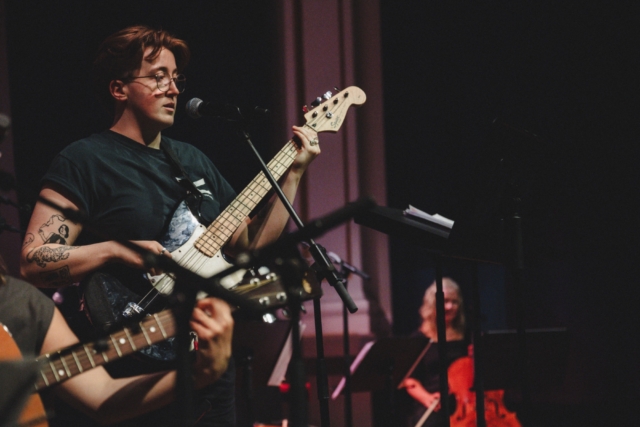 Facilitator Eleri Hewitt playing guitar with the Trinity music group during the Creative Communities summer showcase, 2025.