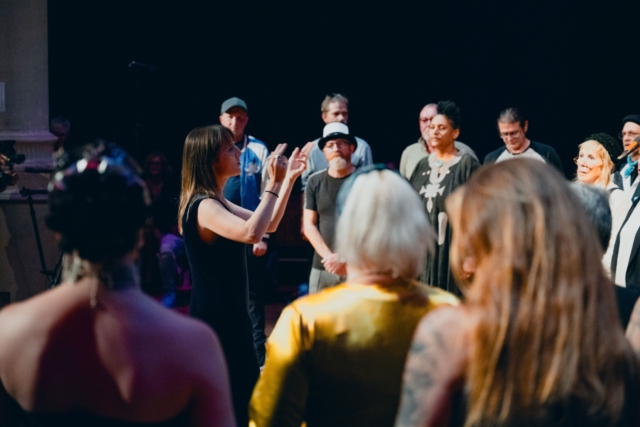 The choir standing in a semi circle singing on stage at Circomedia being led by Sophie.