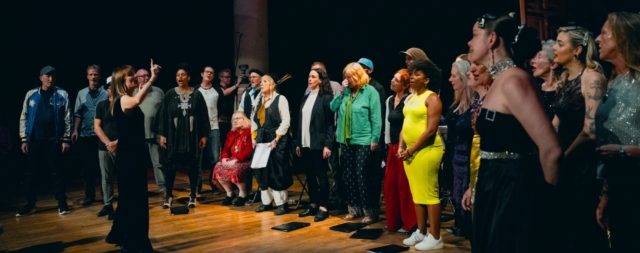 Choir leader, Sophie, holding up hand to indicate one more time through a song.