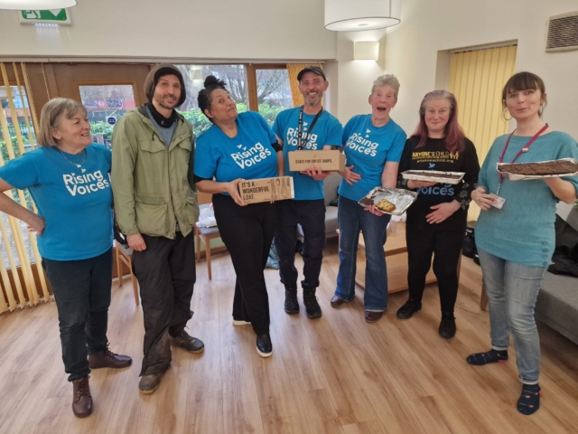 The choir standing in a huddle, smiling and holding cakes after their performance at Cakesmith in 2024.